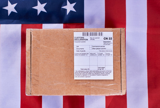 Parcel with Customs declaration form CN22 on American flag background. Gneral view