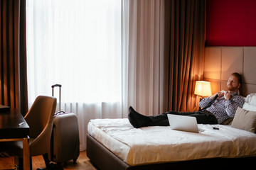 Manager takes a break, lays on the bed. Businessman relaxing in bed with a lap top beside him. 