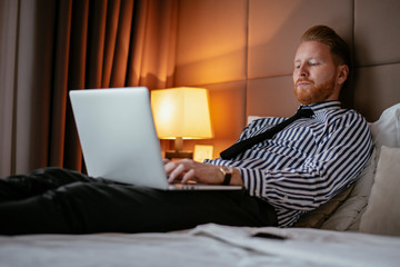 Manager takes a break, lays on the bed. Businessman relaxing in bed with a lap top beside him. 