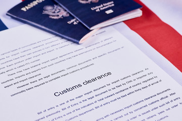 Page of paper with words Customs Clearance next to American passports on American flag background