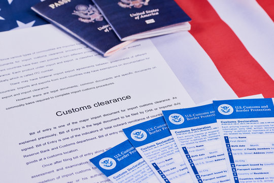 Page of paper with words Customs Clearance next to American passports and Forms of the customs declaration on American flag background