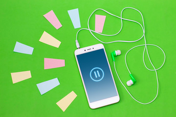 Headphones with a smartphone on a green background and multi-colored stripes - listening to music, concept