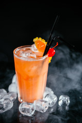 Orange cocktail with fruit on a black smoky background.