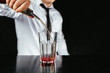 Barman makes a red highball cocktail on a black counter, black background. 