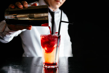 Barman makes a two colored cocktail on a black counter, black background. 