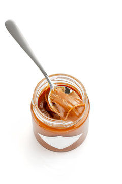Spoon with salted caramel sauce on jar isolated on white