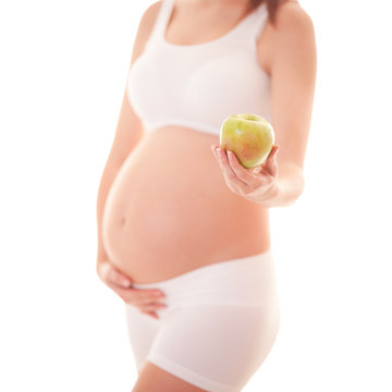 Image of pregnant woman touching her big belly and holding apple in the hand isolated on white background. Close up. Beautiful body of pregnant woman. Motherhood, pregnancy concept. 