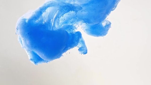 Droplet of blue acrylic paint recorded while dissolving into water, close shot. Abstract background. Acrylic cloud swirling in liquid. Abstract pattern. Blue ink in water. Blurred background