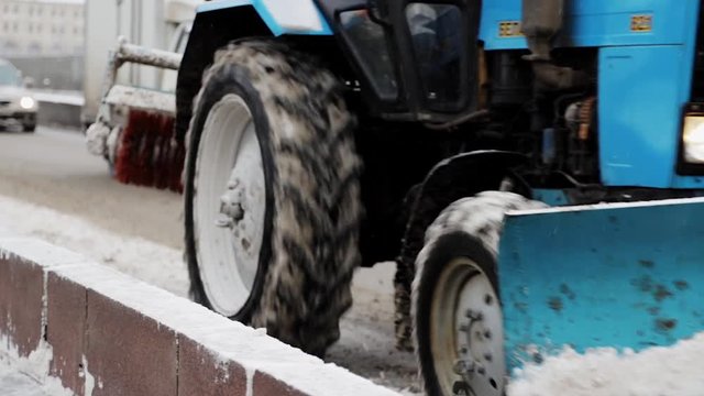 Snowplow moving driving along the road on the bridge. Gimbal shot of blue tractor snow-cleaning machine passing by slowly at daylight not cleaning snow.