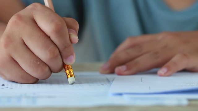 Students holding pencil eraser while taking exams, examination room, writing answer optical form in high school classroom, view of having test in class on seat rows, Education literacy concept.
