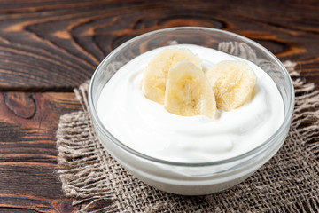Banana and yogurt on dark wooden background.