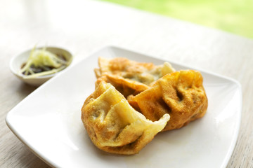 Chinese dumplings snack with soy sauce and ginger. On wooden table and green grass background.