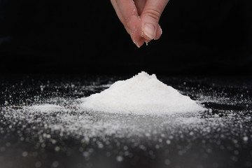 in the fingers of a young woman a pinch of salt, which she pours down on a hill of salt. Image on black background. Concept - salt-free diet.