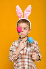 Obraz na płótnie Canvas Portrait of cute little child boy with Easter bunny ears holding colorful eggs on yellow background. Happy easter
