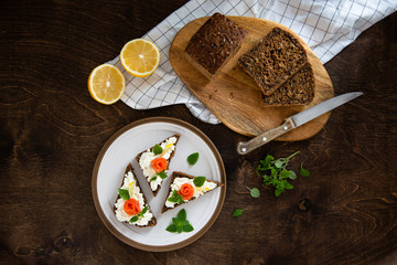 Sandwich with cereals bread, salmon, fresh cheese, basil and lemon on dark rustic background. Top view, copy space