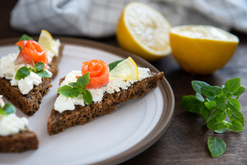 Bread with fresh salmon fillet, cream cheese and lemon on white plate, side view. Copy space, close up