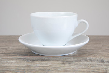 White mug and saucer on a wooden table.