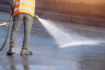 Worker cleaning driveway with gasoline high pressure washer splashing the dirt, asphalt road. High...