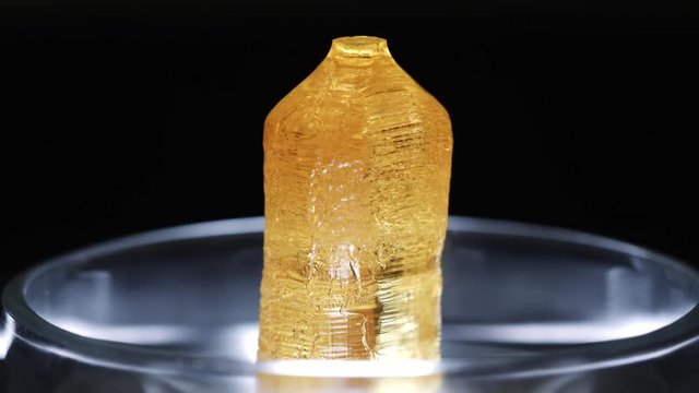 Close-up of transparent yellow mineral standing in a glass laboratory utensils on a black background. Stock footage. Chemistry experiments
