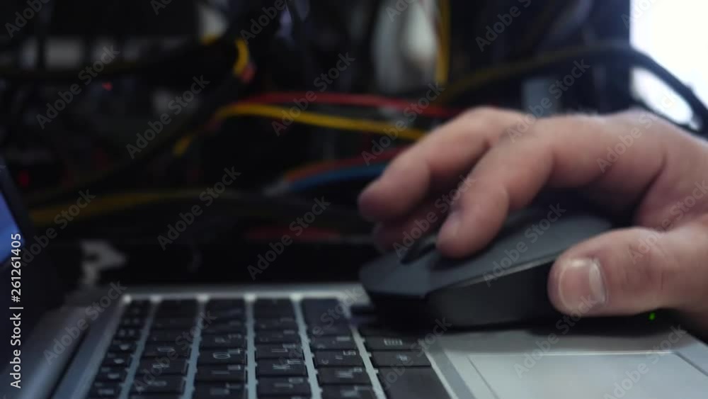 Poster close-up of system administrator hand working on laptop and clicking computer mouse in data center. 