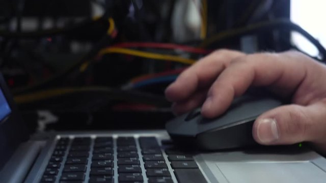 Close-up of system administrator hand working on laptop and clicking computer mouse in data center. Stock footage. Administrator's working