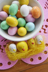 Obraz na płótnie Canvas Easter colorful background with Easter chocolate eggs in a bowl and little chicken decoration on wooden table