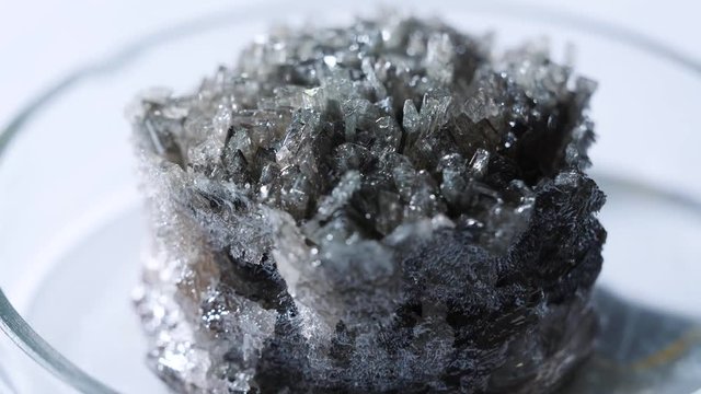 Close-up of grey naturally occurring mineral standing in a glass laboratory utensils on the table. Stock footage. Chemistry experiments