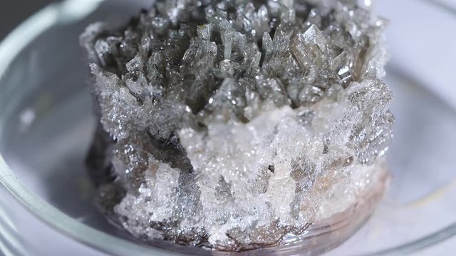 Close-up of grey naturally occurring mineral standing in a glass laboratory utensils on the table. Stock footage. Chemistry experiments
