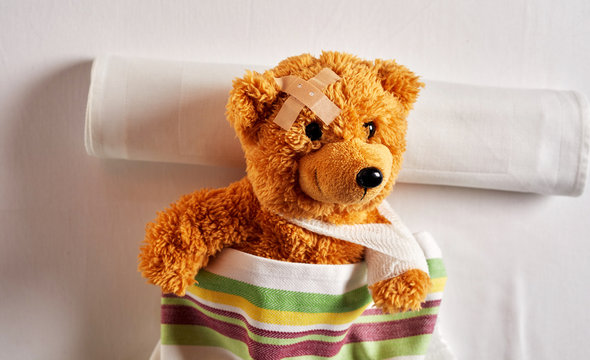 Little brown teddy bear lying in a hospital bed