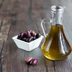 Olive oil in a glass jug on a brown wooden background. Healthy Food. Mediterranean Kitchen.