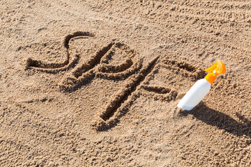 Sun protect factor. SPF word written on the sand and white bottle with suntan cream. Skin care concept background