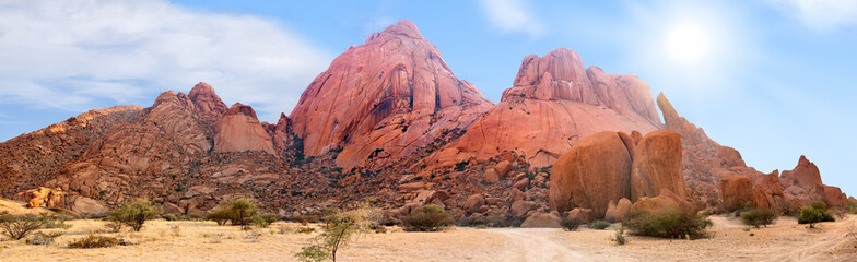Spitzkoppe mountains range panoramic view on blue sky, clouds and bright sun background, red...