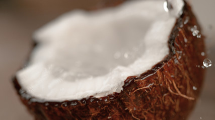 MACRO: Cinematic shot of water droplets splashing into the ripe brown coconut.