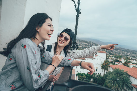 two asian young girls travelers sightseeing view from Santa Barbara County Courthouse usa. beautiful sister showing friends view pointing finger cheerful smiling enjoy city town view on blue sky.