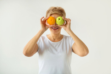 beautiful aged woman with short haircut in a white t-shirt with an apple and an orange on a white background