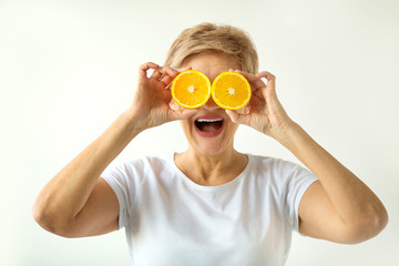 beautiful aged woman with a short haircut in a white T-shirt with oranges in her hands on a white background