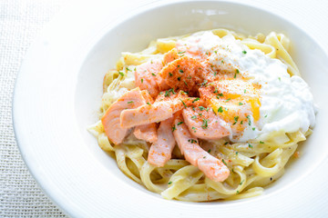 Fettucine with salmon, egg and parmesan cheese, served on white plate..