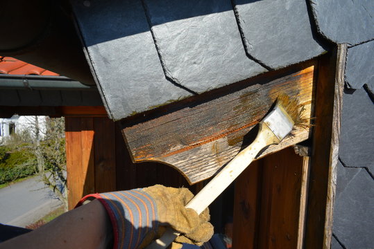 Streichen verwitterter Dachbalken auf der Wetterseite mit Pinsel und Holzschutzlasur
