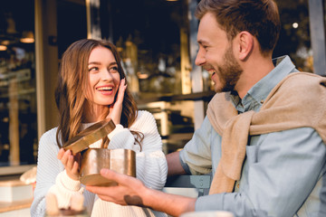 surprised young woman looking at handsome boyfriend holding heart-shape box