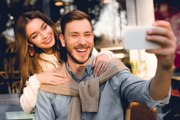 selective focus of happy man taking selfie with cheerful girlfriend