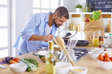 Smiling and confident chef standing in a large kitchen tasting 