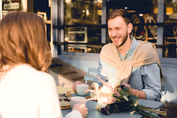 happy man smiling while looking at young woman in cafe