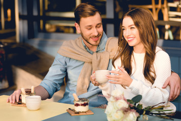 cheerful man looking at cup in hands of happy girlfriend in cafe