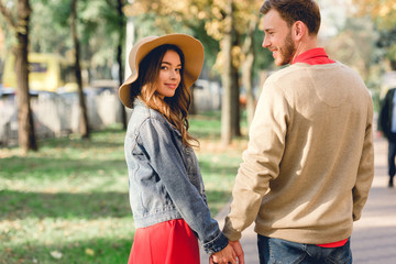 Fototapeta premium handsome man looking at attractive girlfriend in hat while holding hands in park