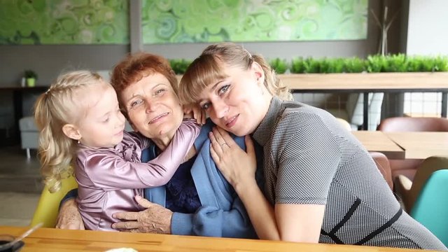 Adult daughter and little granddaughter kiss their grandmother. Women of  same family hug and kiss. Little girl granddaughter kisses her grandmother, a beautiful young daughter hugs her mother.