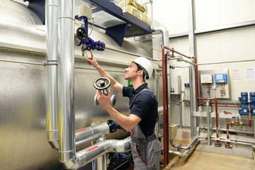 Industriearbeiter in Arbeitskleidung und Helm bedient eine Anlage in einer technischen Fabrik //...