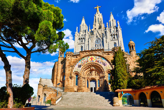 Barcelona, Spain. Tibidabo Cathedral. Temple of the Sacred Heart of Jesus at Mount Tibidabo. High pine-tree tree and blue sky with cloud of summer day. Famous landmark in Catalonia, Espana.
