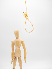Miniature wooden doll stands near hanging rope and watch on gallow noose. 