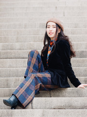 Beautiful young brunette woman sitting on steps and smiling at camera. Outdoor fashion portrait of glamour young Chinese stylish lady. Emotions, people, beauty and lifestyle concept.