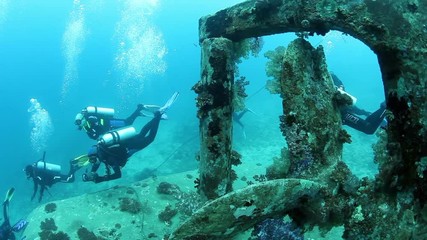 Ship screw of underwater wreck and group of divers on sunken ship covered in coral on the Pacific Ocean seabed in Fiji.